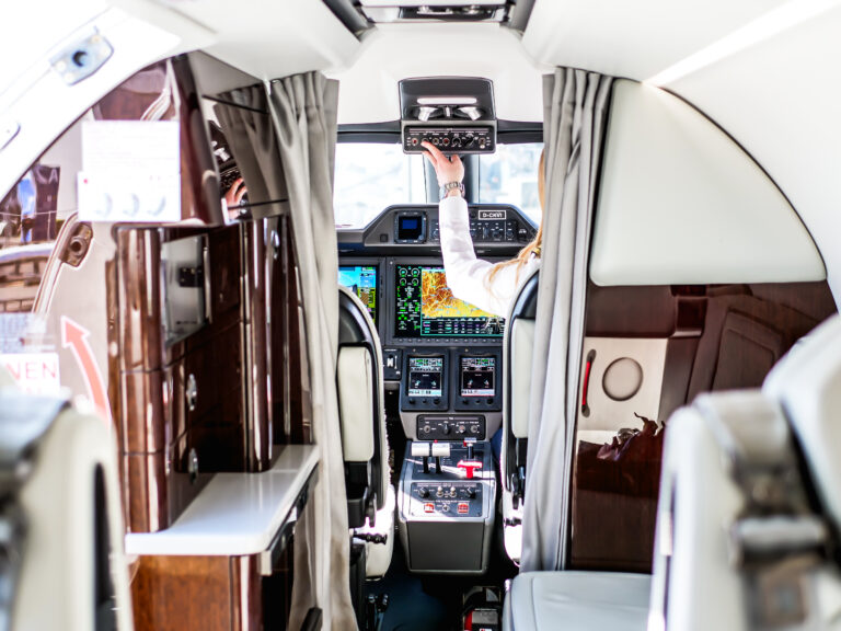 A woman sits in the cockpit of a private jet, focused on the controls and instruments in front of her.