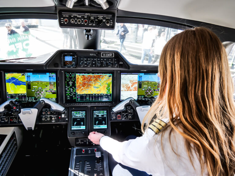 A woman operating a plane cockpit, with various screens showing navigation and flight information.